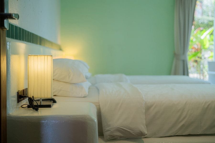 A neatly made bed with white sheets and a lamp beside it, symbolizing comfort and tranquility in rehab Thailand.